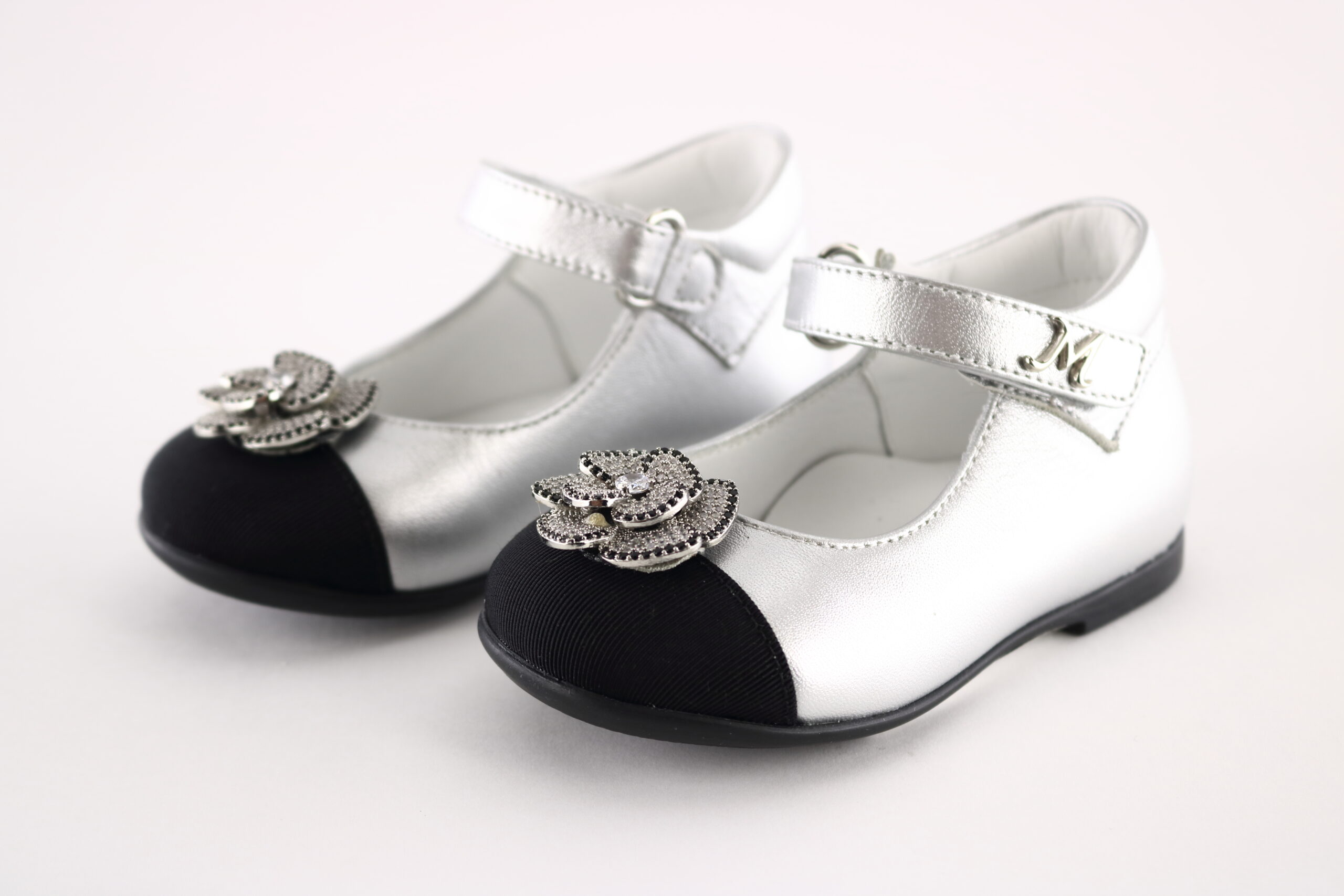 Missouri art. 2020A – Girls’ Mary Jane flat in silver metallic leather with black patent toe cap, jewel flower application and “M” logo strap.